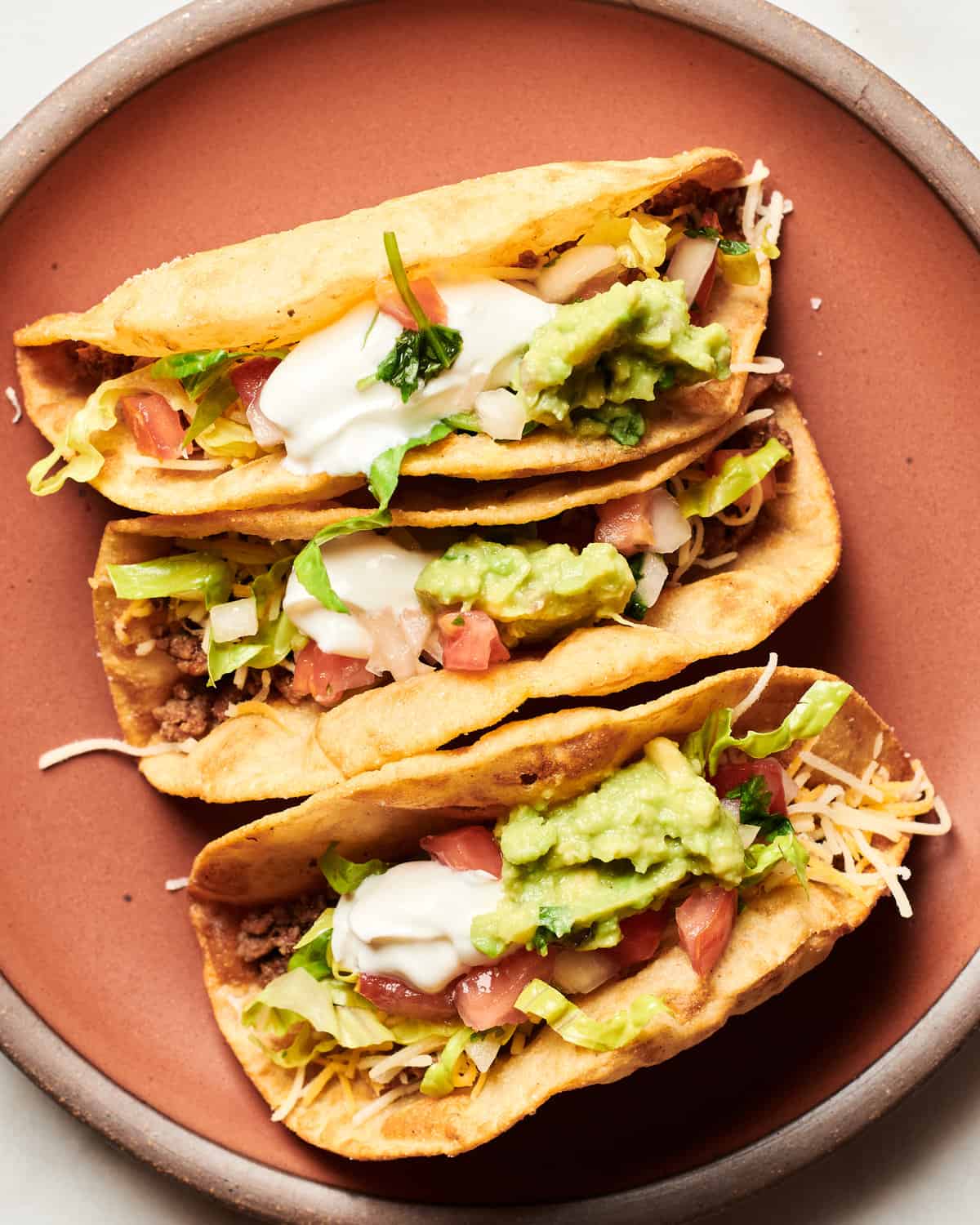 Ground Beef Tacos topped with sour cream, guacamole, pico de gallo, shredded lettuce on a orange plate.