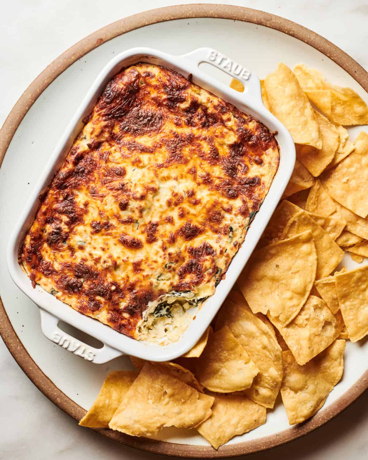 Spinach Artichoke Dip with browned top served on a plate with chips. 