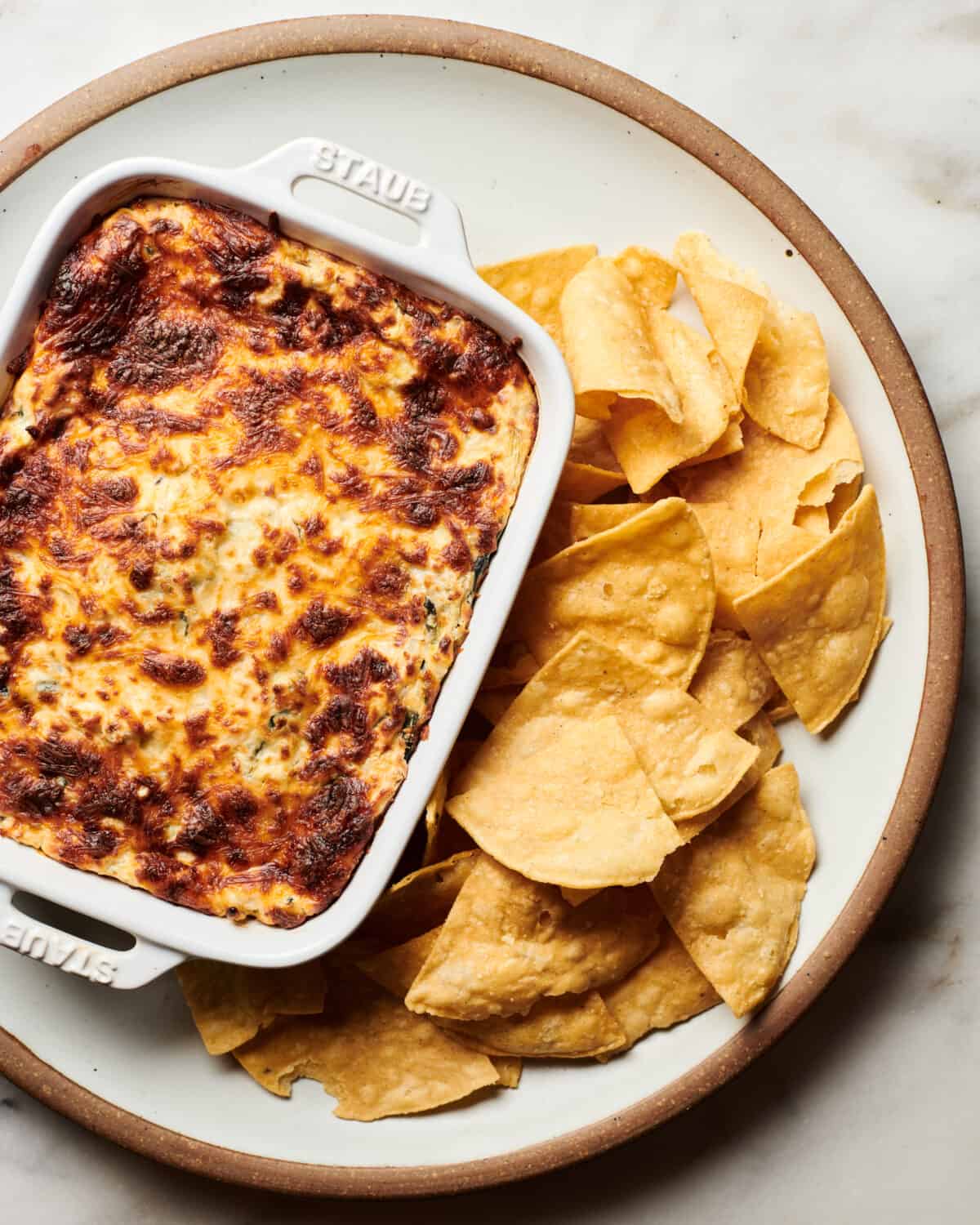 Spinach Artichoke Dip with browned top served on a plate with chips. 