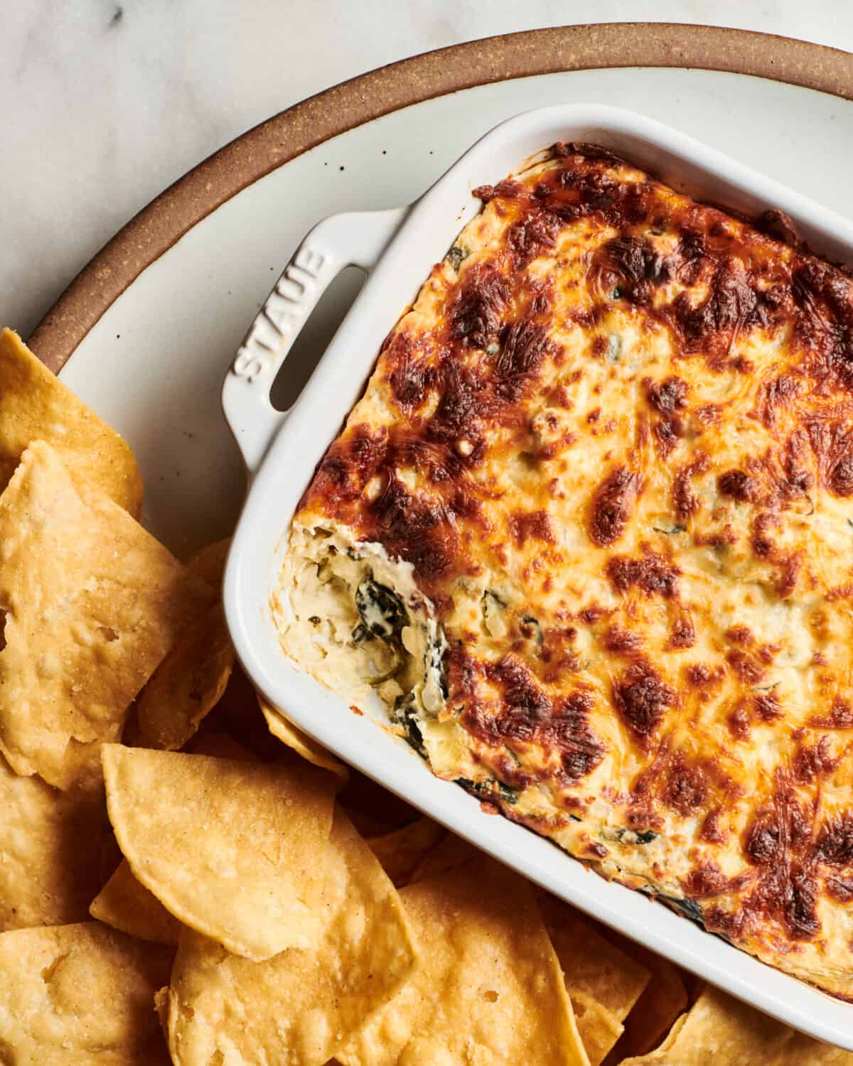 Spinach Artichoke Dip with browned top served on a plate with chips. 