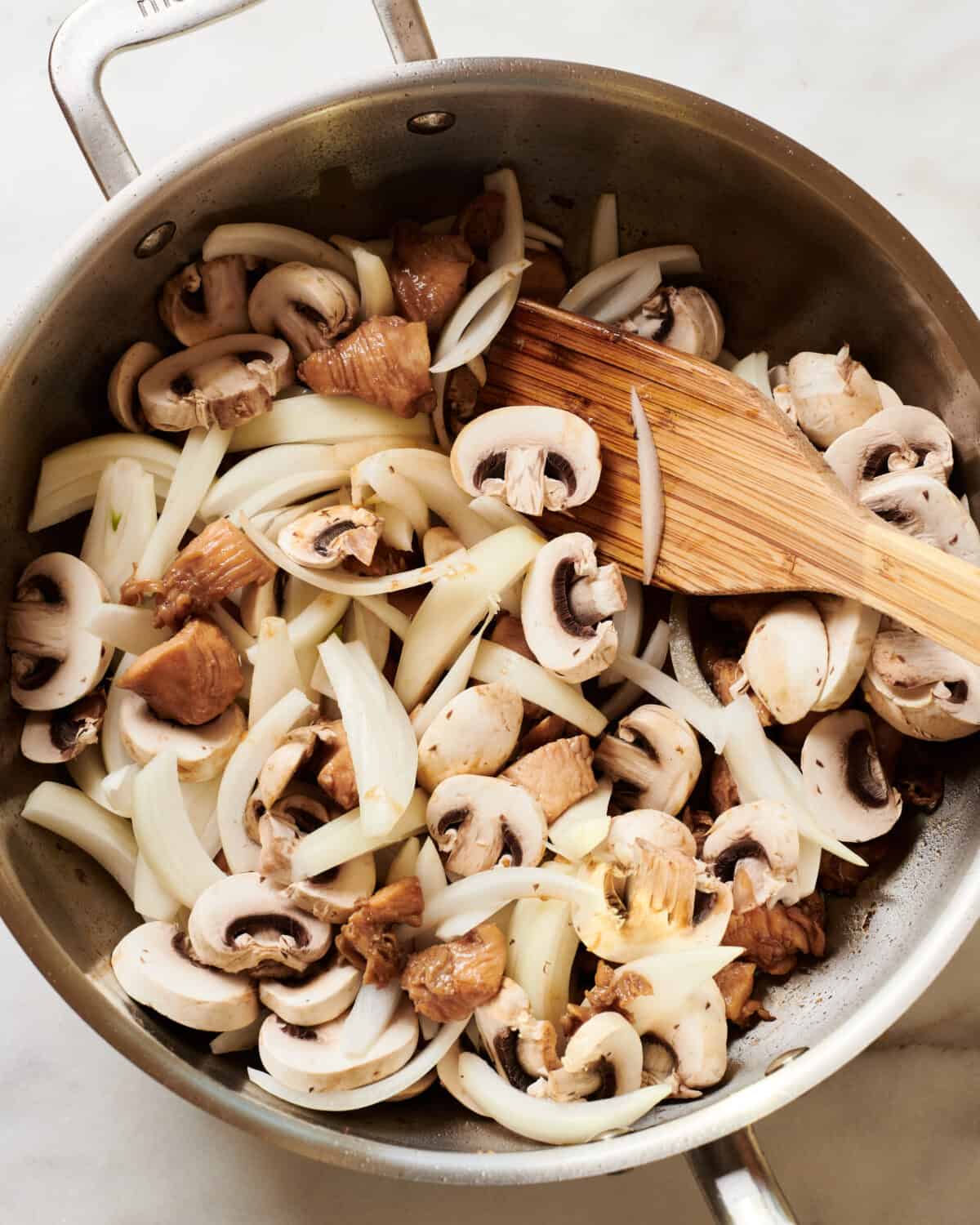 Raw mushrooms and onions being added to pan. 