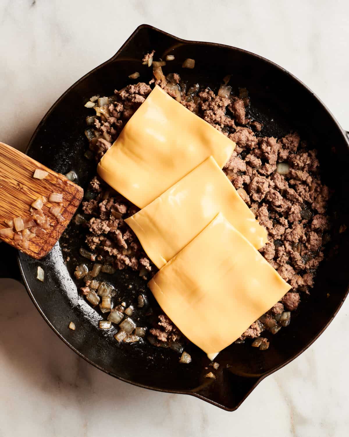American cheese on top of ground beef in a pan. 