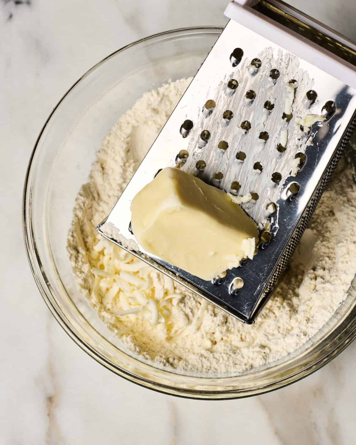 Butter being grated into a bowl. 