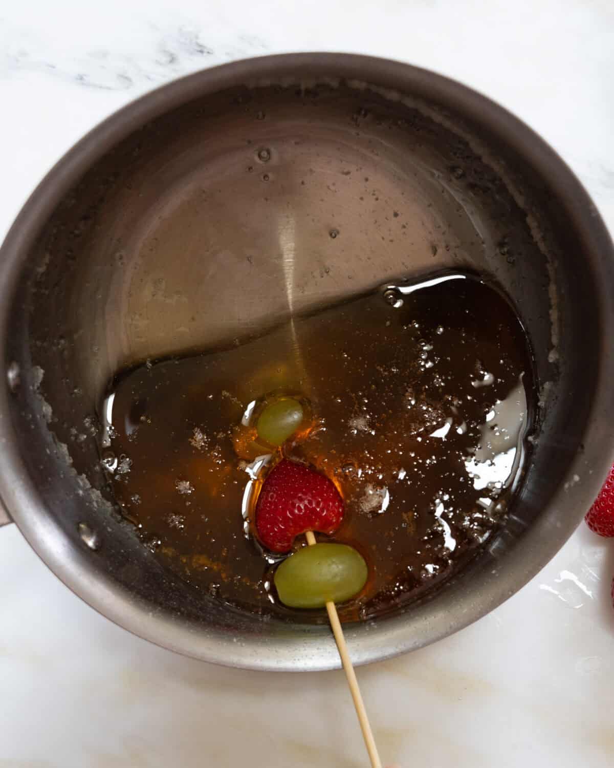 Strawberry and grapes being dunked in candied sugar. 