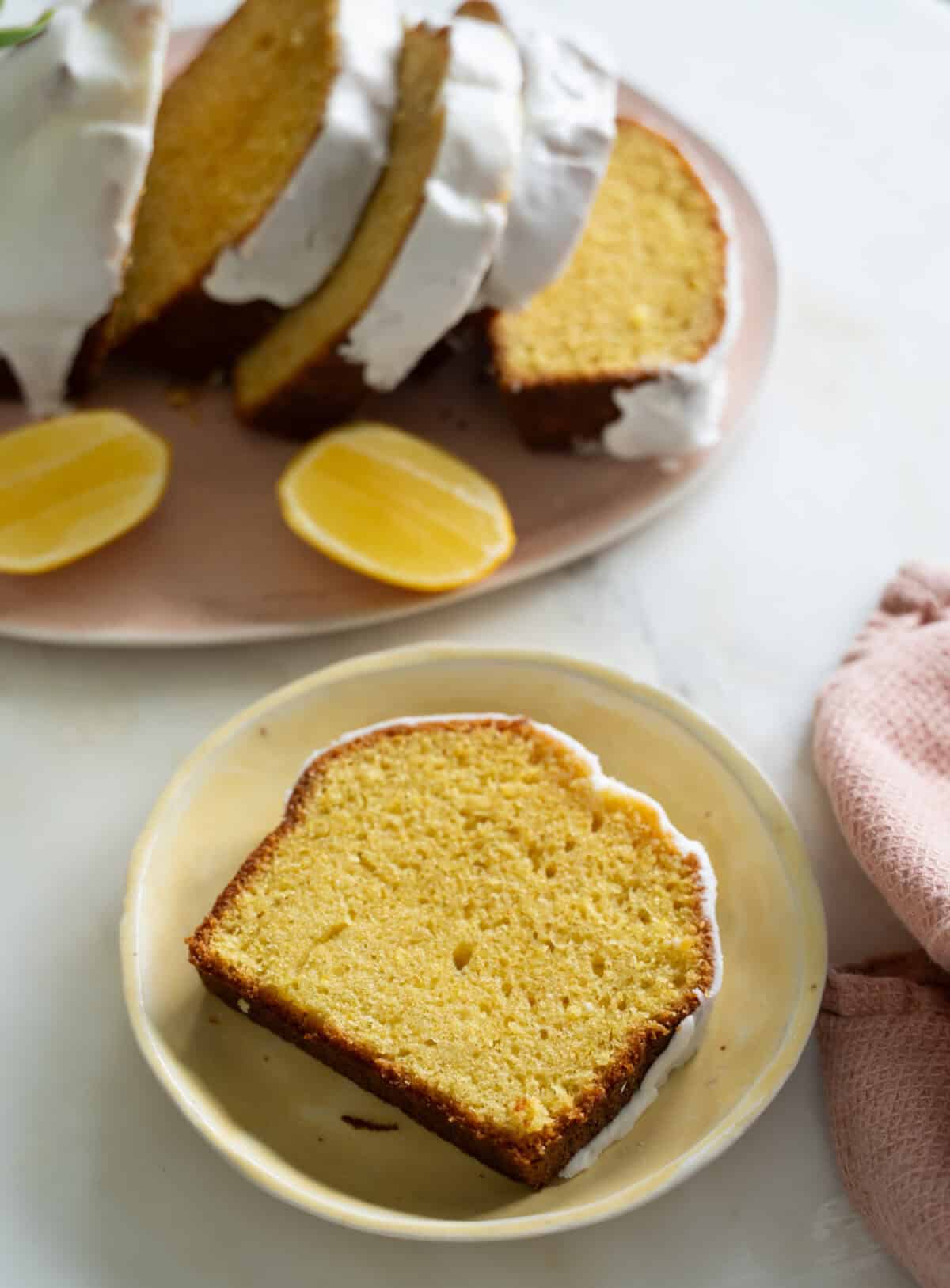 Starbucks Copycat recipe of this Lemon Loaf with glaze on top. A slice is on a yellow plate with the rest of the loaf in the background.