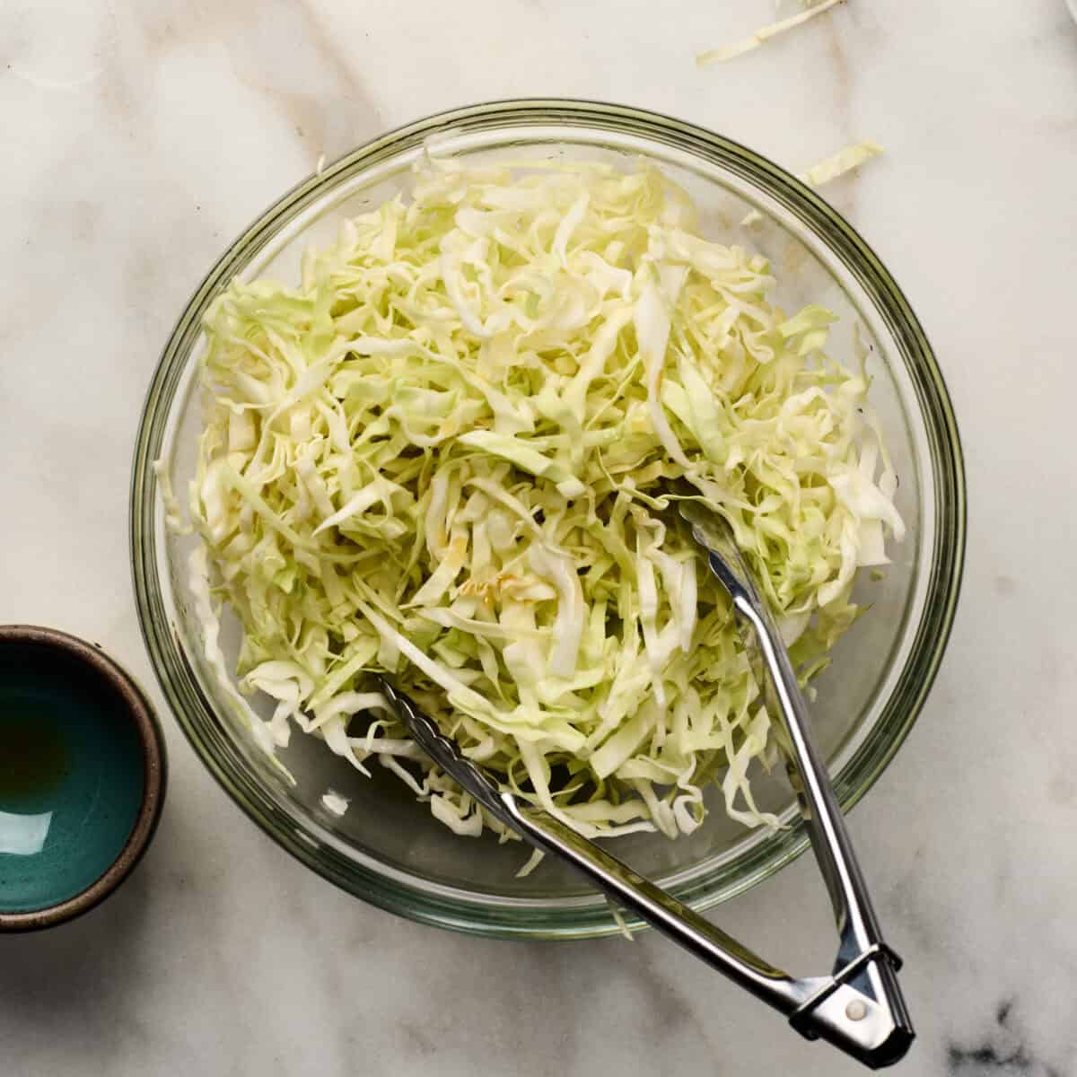 Cabbage slaw in a bowl with tongs. 