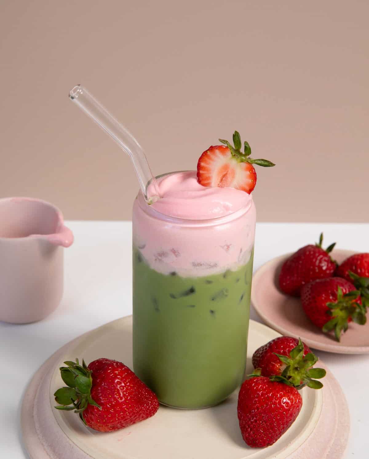 Strawberry Matcha Latte with strawberries on the side with a glass straw. 