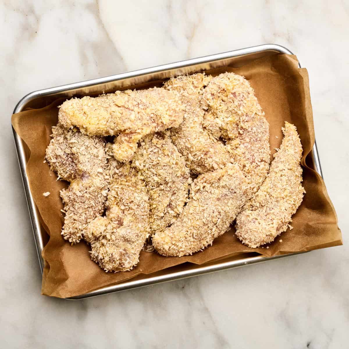 Chicken all breaded on a baking sheet. 