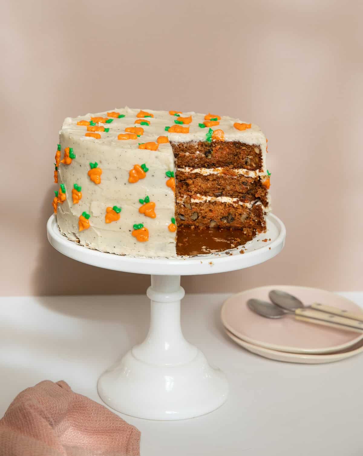 Carrot Cake on a cake stand with plates and spoons next to it.