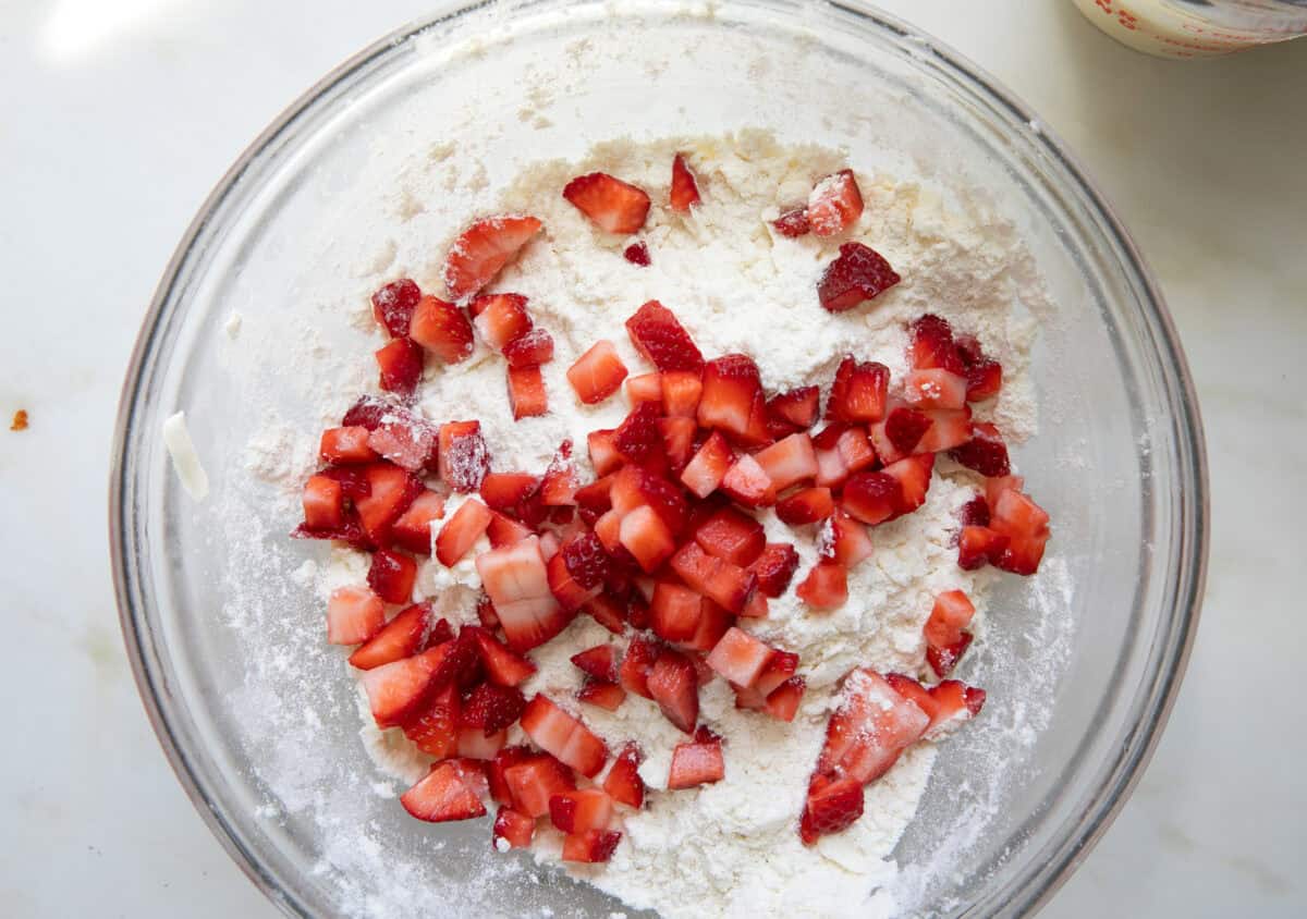 Diced strawberries being tossed in the dry ingredients in a bowl. 