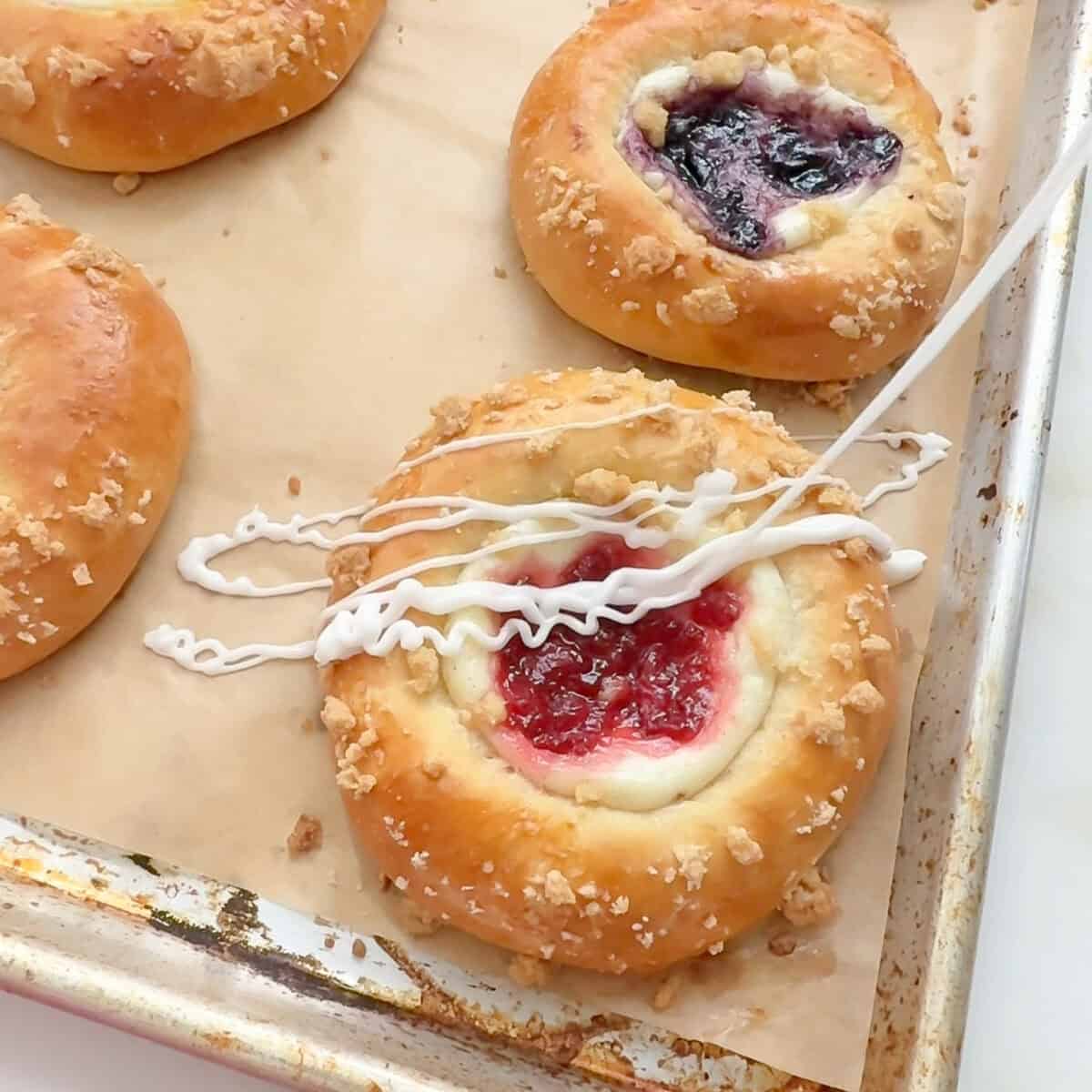 Drizzling icing onto berry cheese danish.