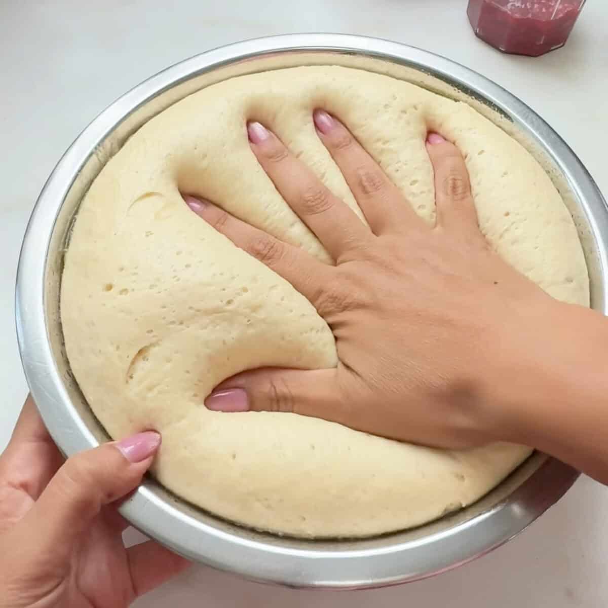 Hand pressing down risen dough in bowl.