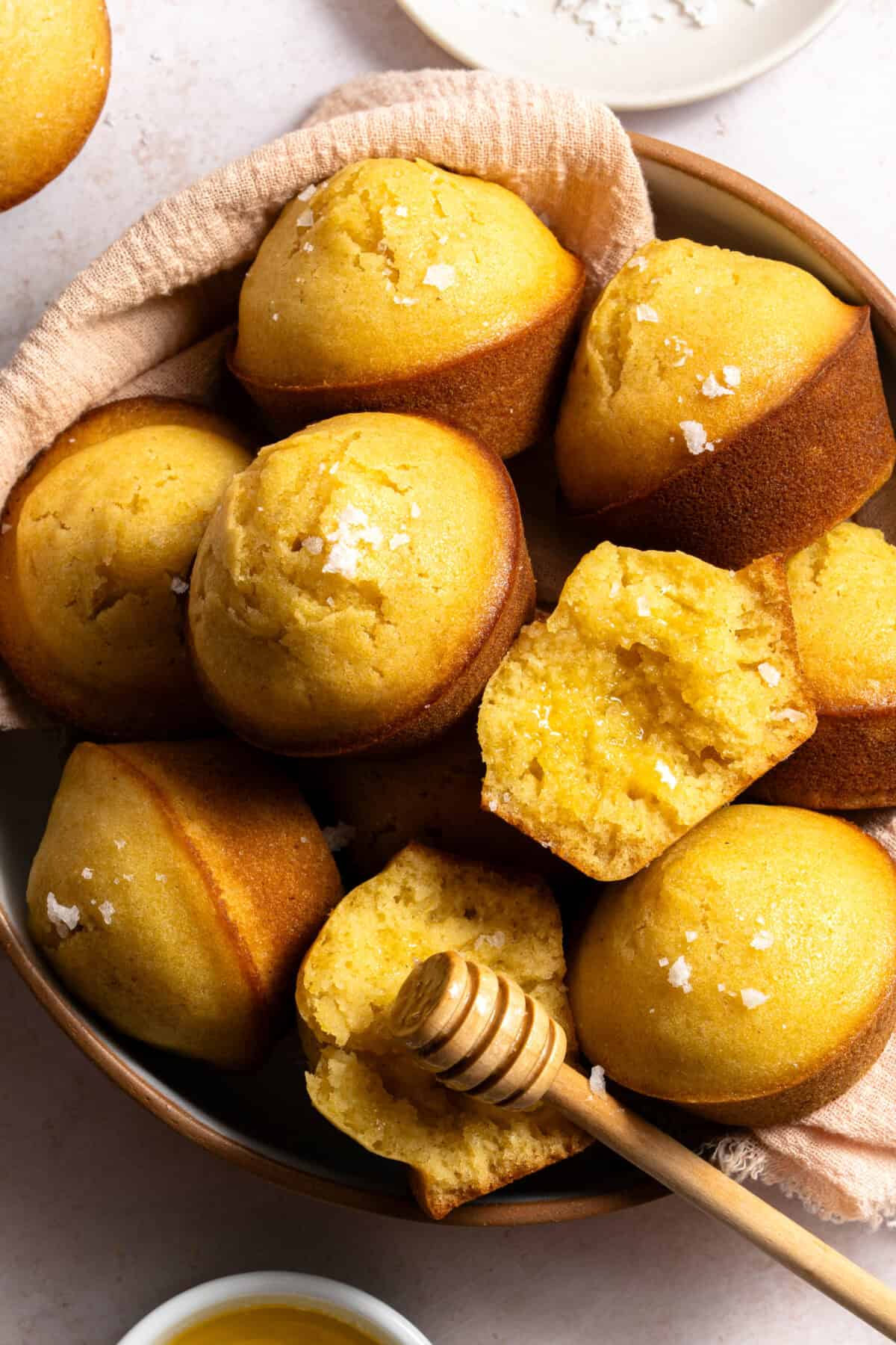 Honey cornbread muffins in a bowl with honey butter glaze and flaky sea salt.