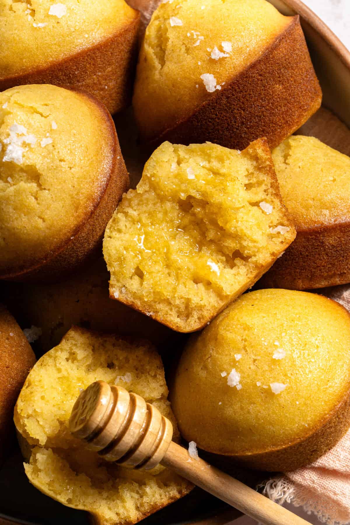 Close up bowl of honey cornbread muffins with honey butter glaze and flaky sea salt.