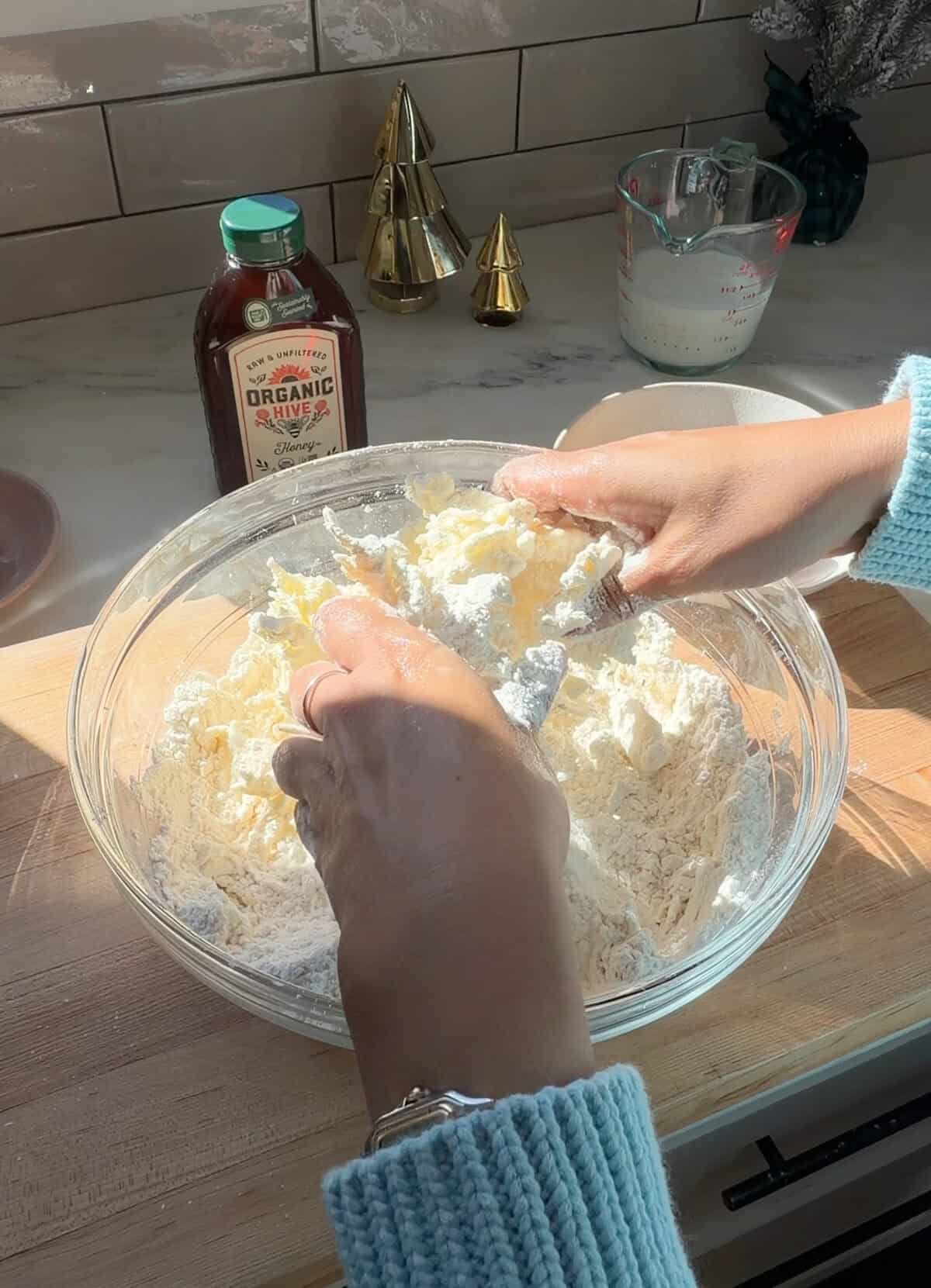 Hands breaking up butter into biscuit dry ingredients.