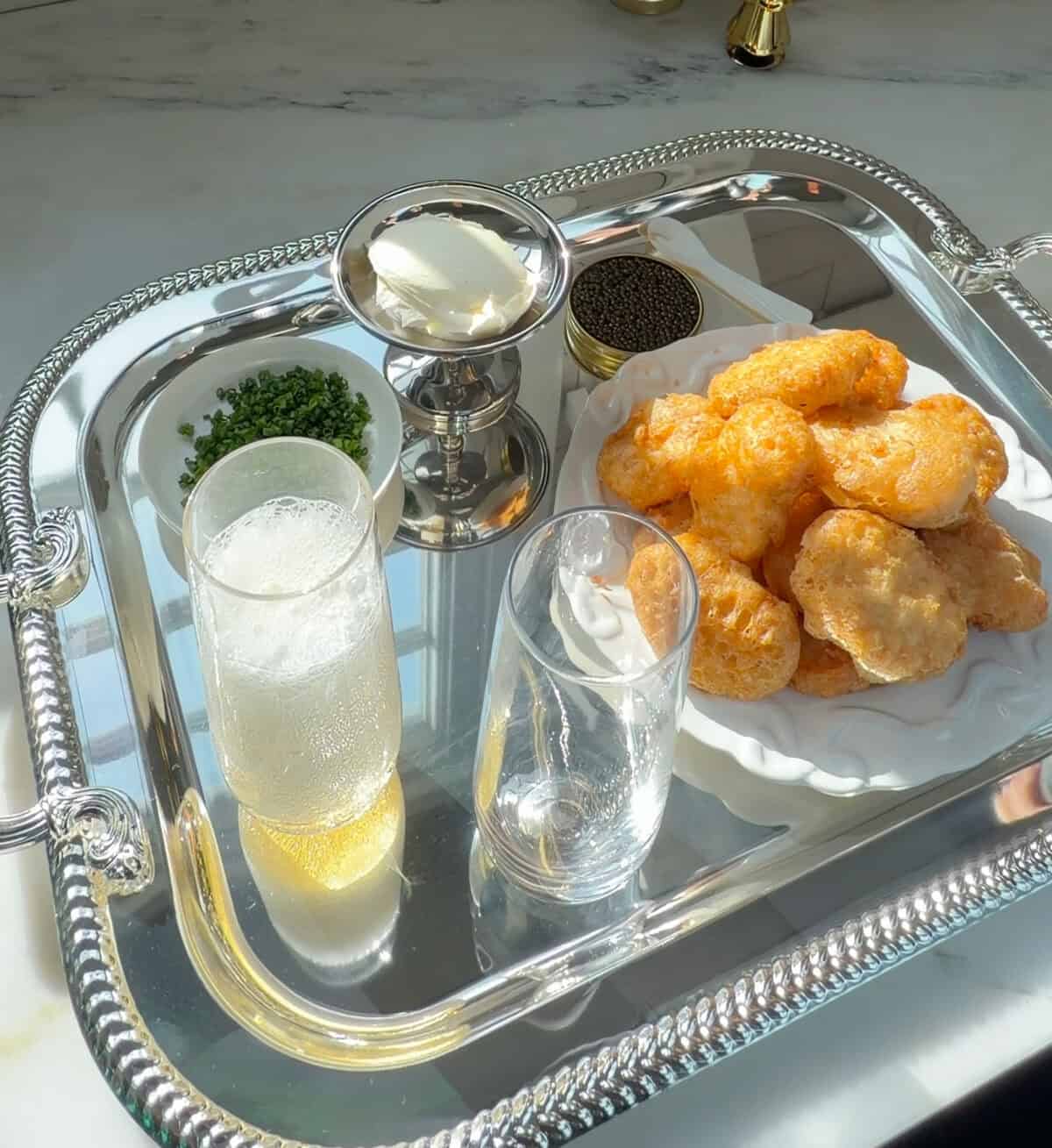 चाइव्स, क्रेम फ्रैच और कैवियार के साथ चांदी की थाली में घर का बना चिकन नगेट्स।