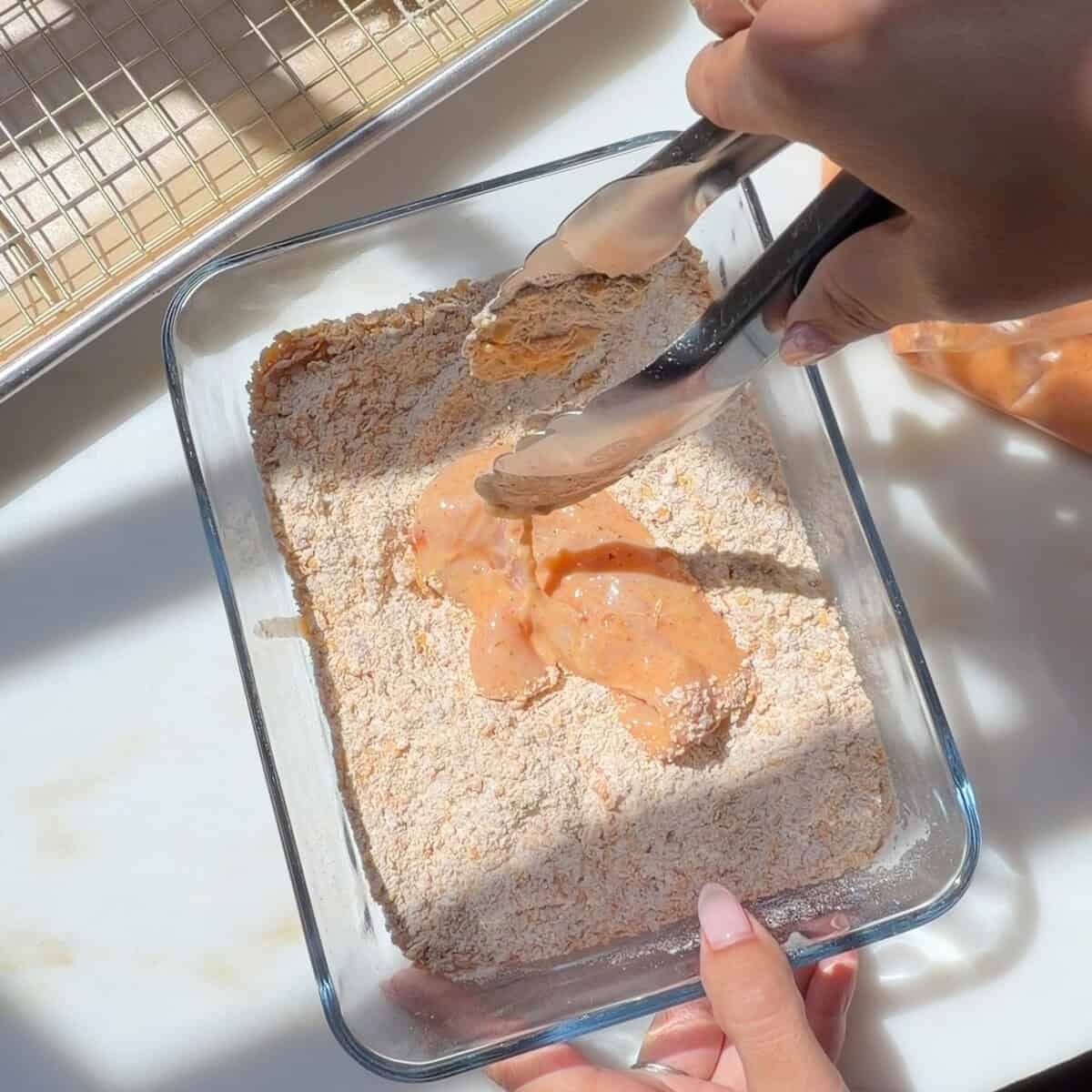 Chicken tenders in dredge in container.