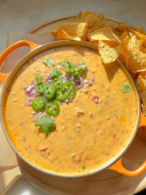 Rotel dip garnished with cilantro, jalapeño, and red onion with tortilla chips on the side.