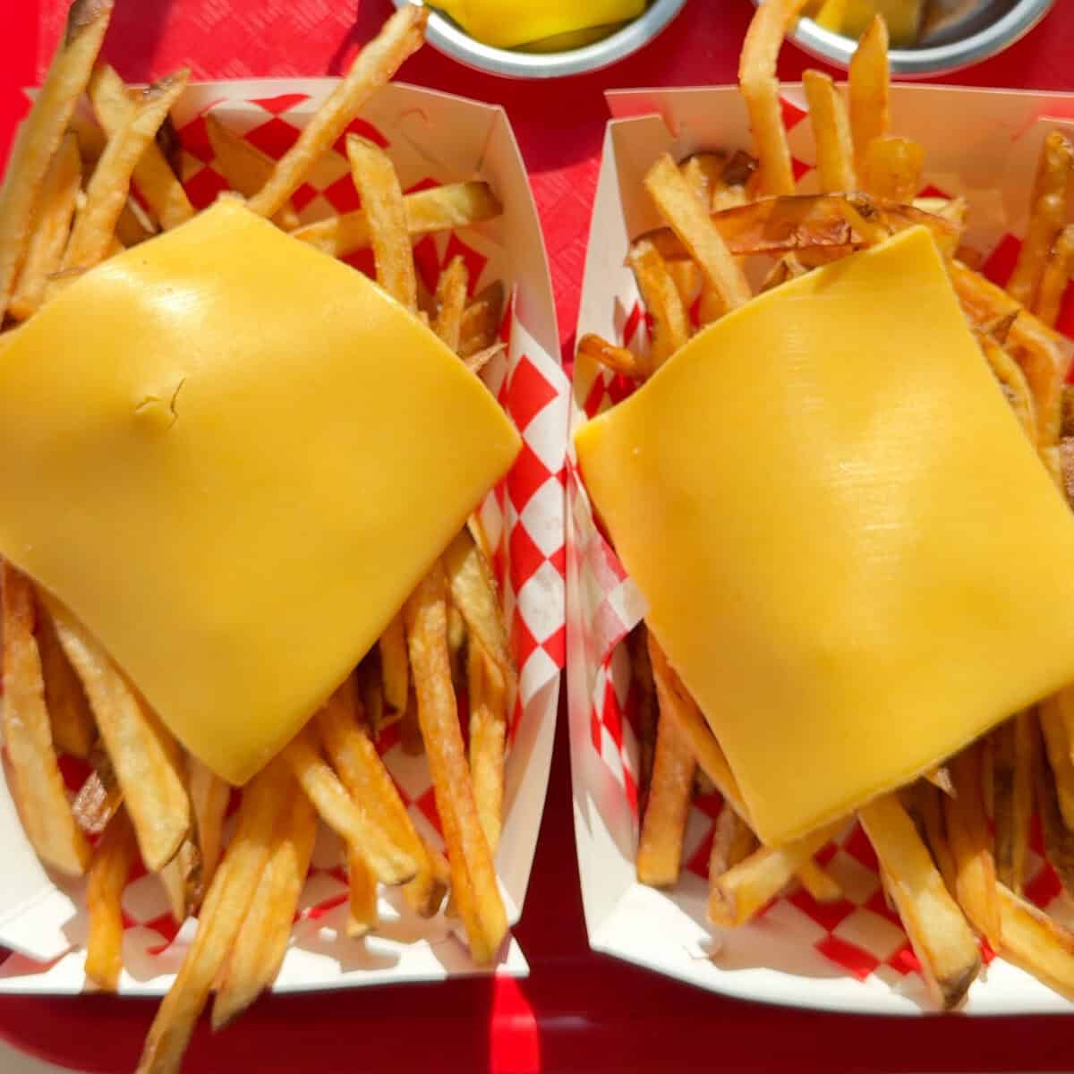 Two baskets of fries with American cheese on top.