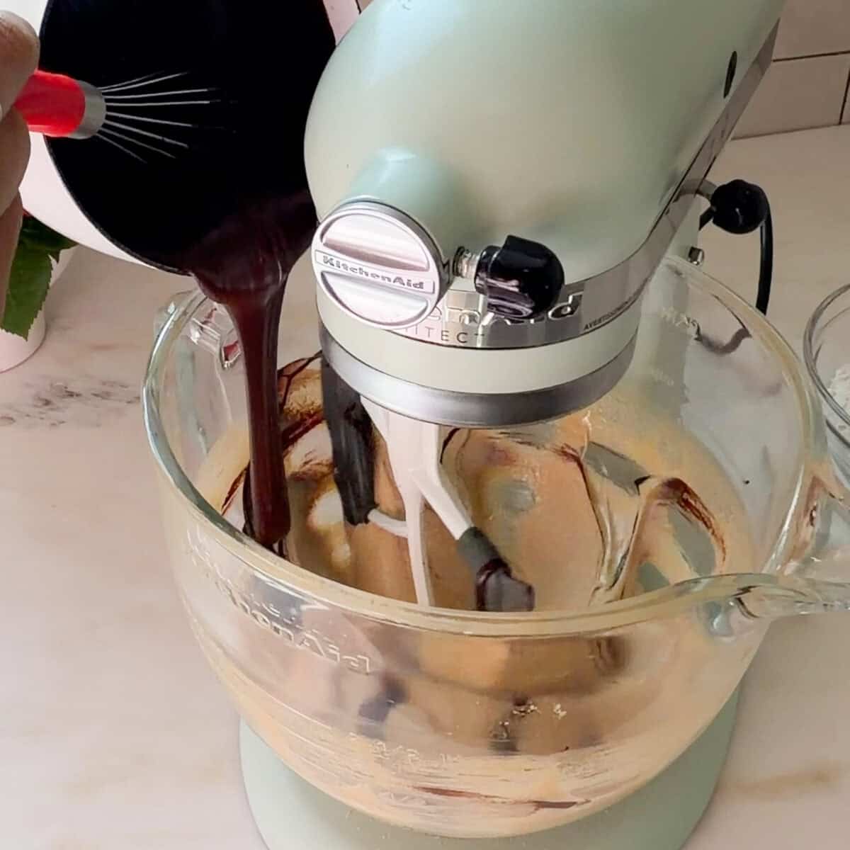 Adding melted chocolate to whipped egg mixture in stand up mixer.