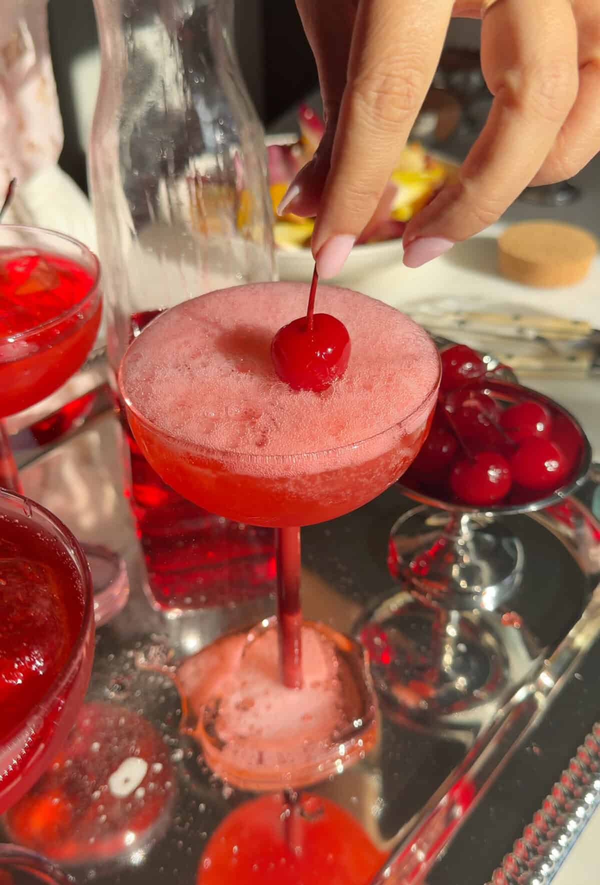 Hand placing cherry on fizzling Dirty Shirley Cocktail.