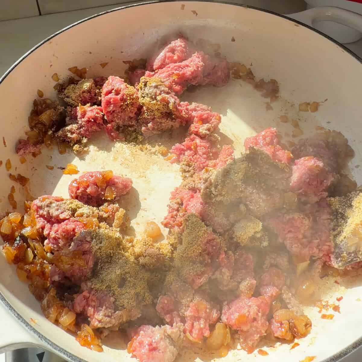 Ground beef cooking with spices in pan.