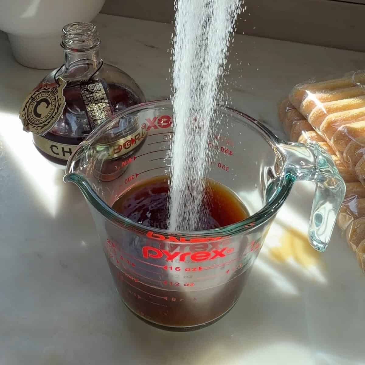 Sugar being added to coffee in measuring cup.