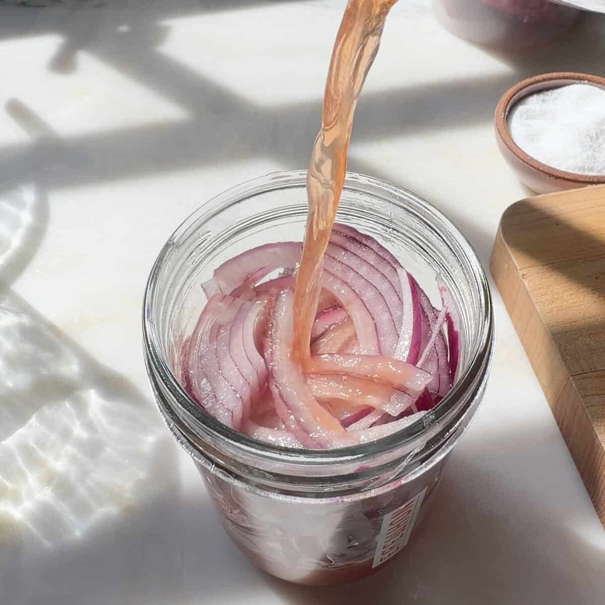 Pouring vinegar mixture over sliced red onions in jar.