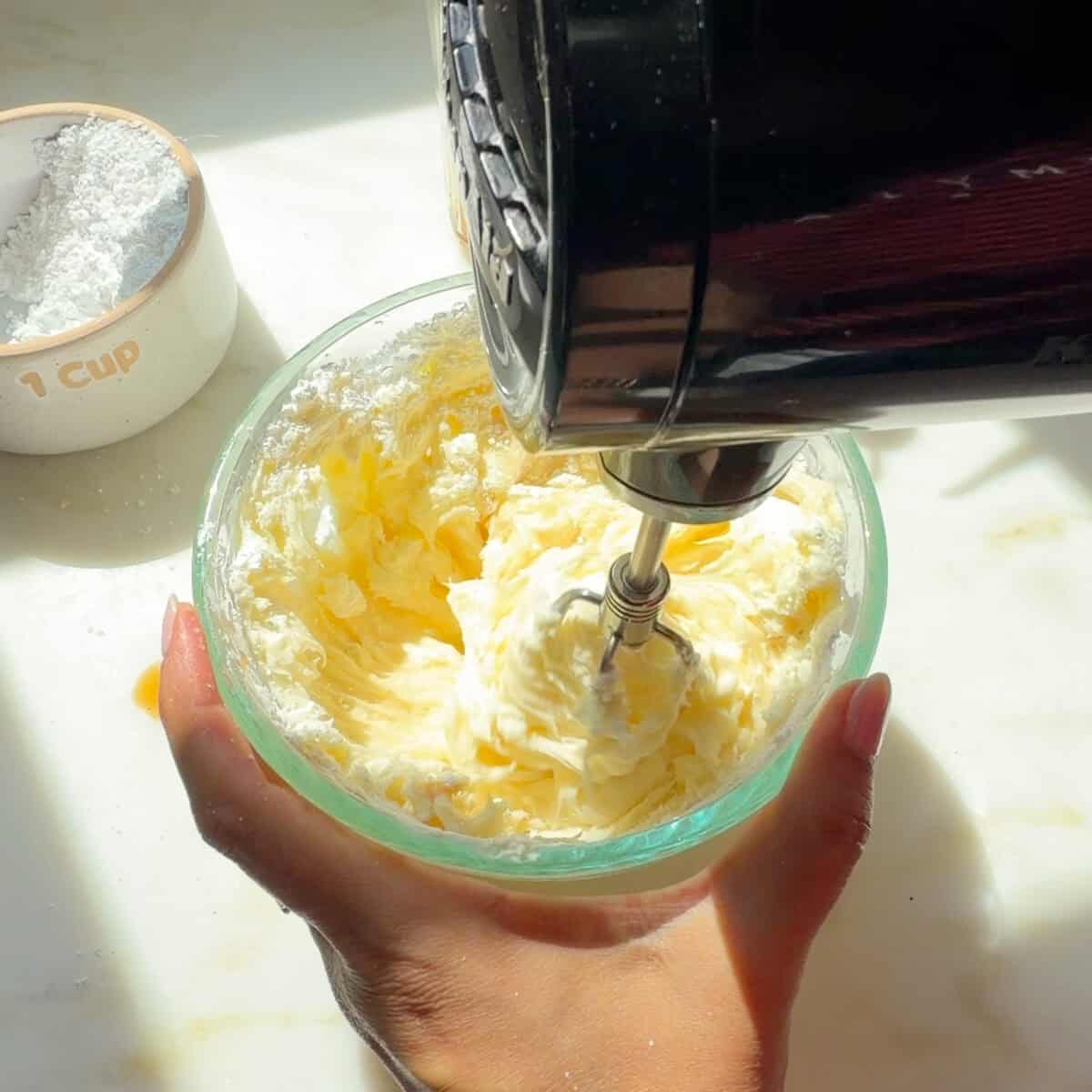 Cream cheese frosting being beaten with hand mixer.