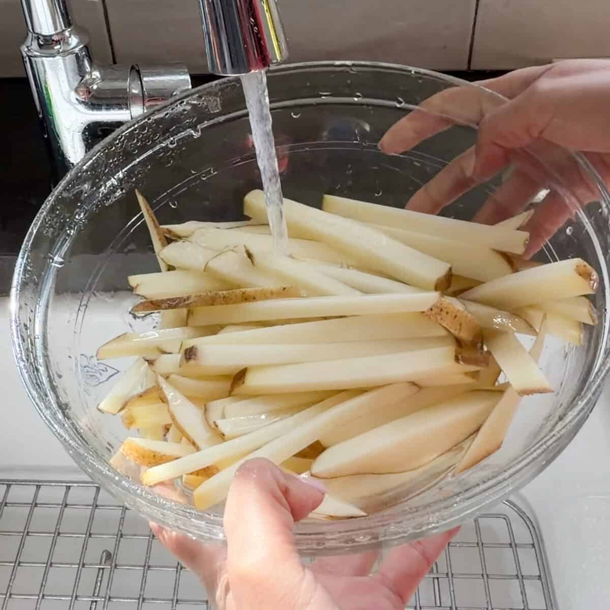 French fry cut potatoes being rinsed under cold water.