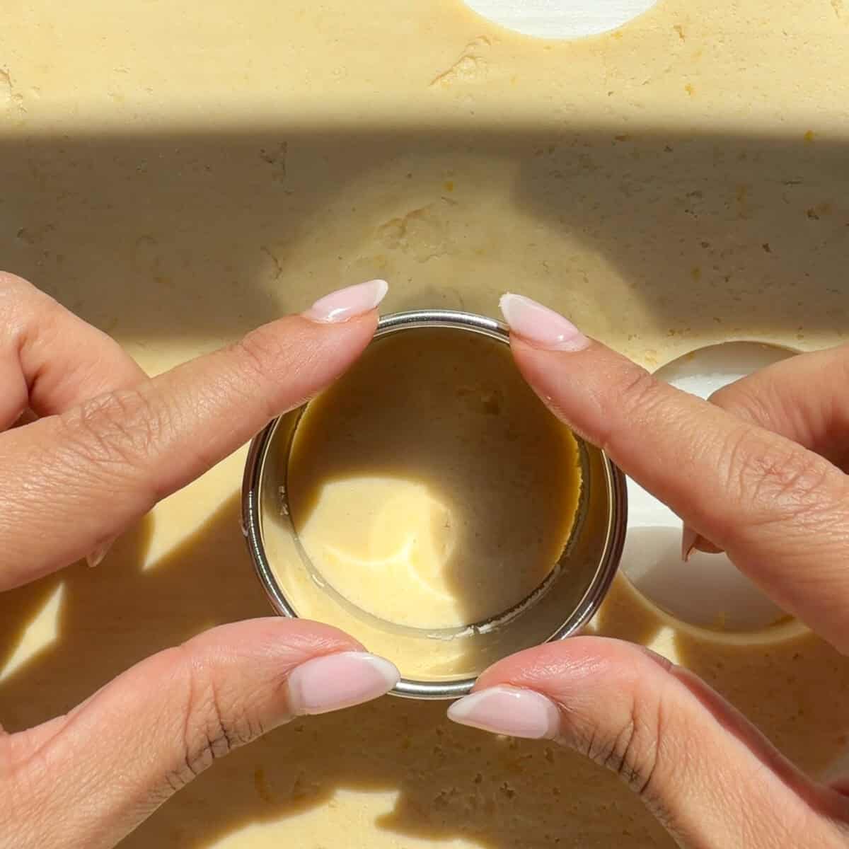 Hands stamping out cookies from rolled out cookie dough.
