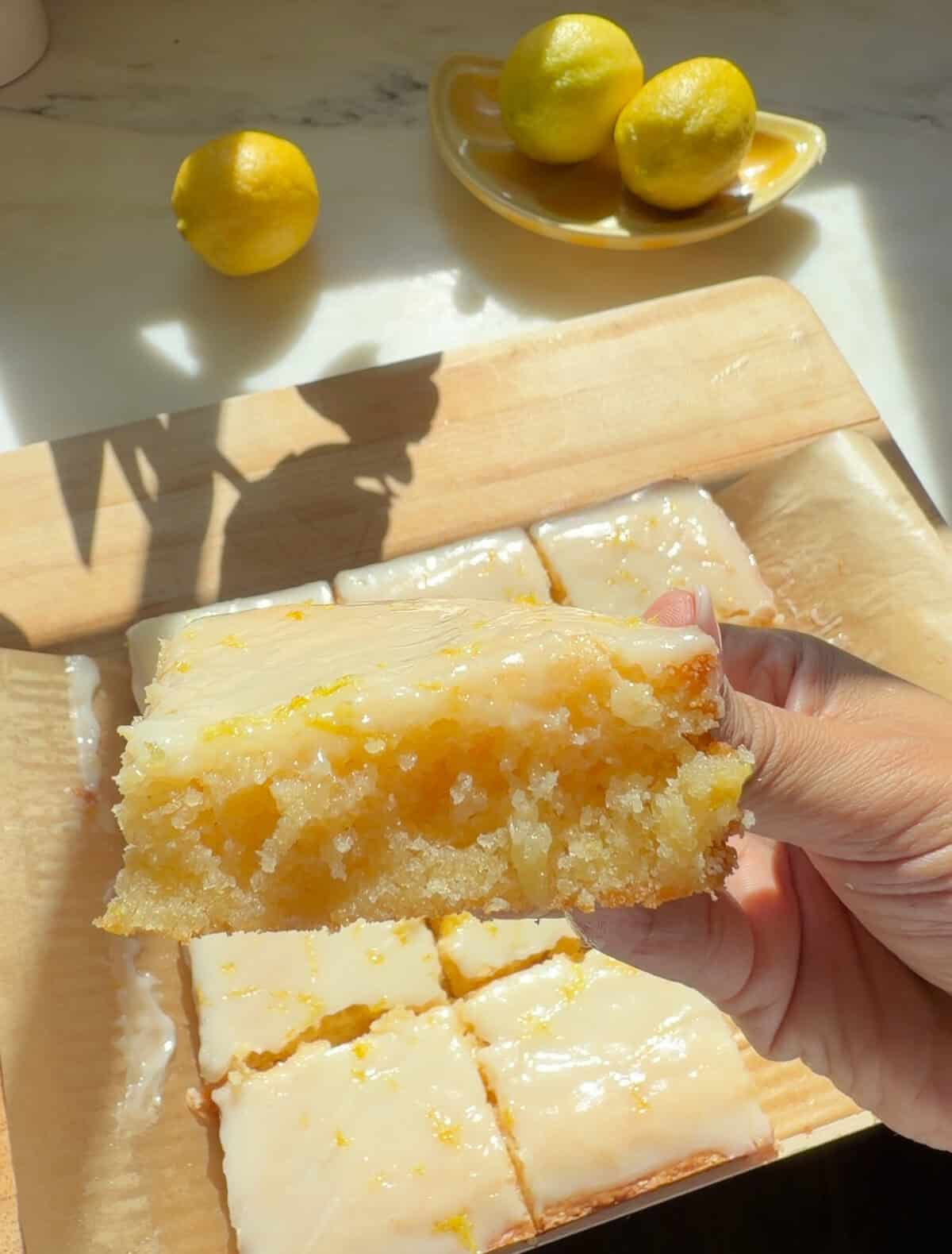 Hand holding slice of Lemon Brownie with white chocolate lemon glaze.