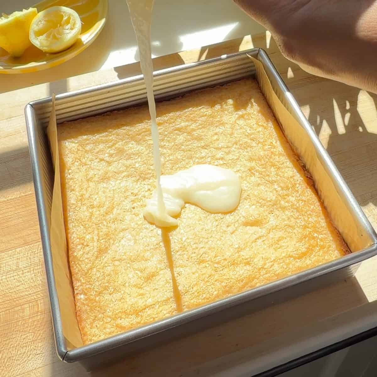 Pouring white chocolate lemon glaze over lemon brownies.