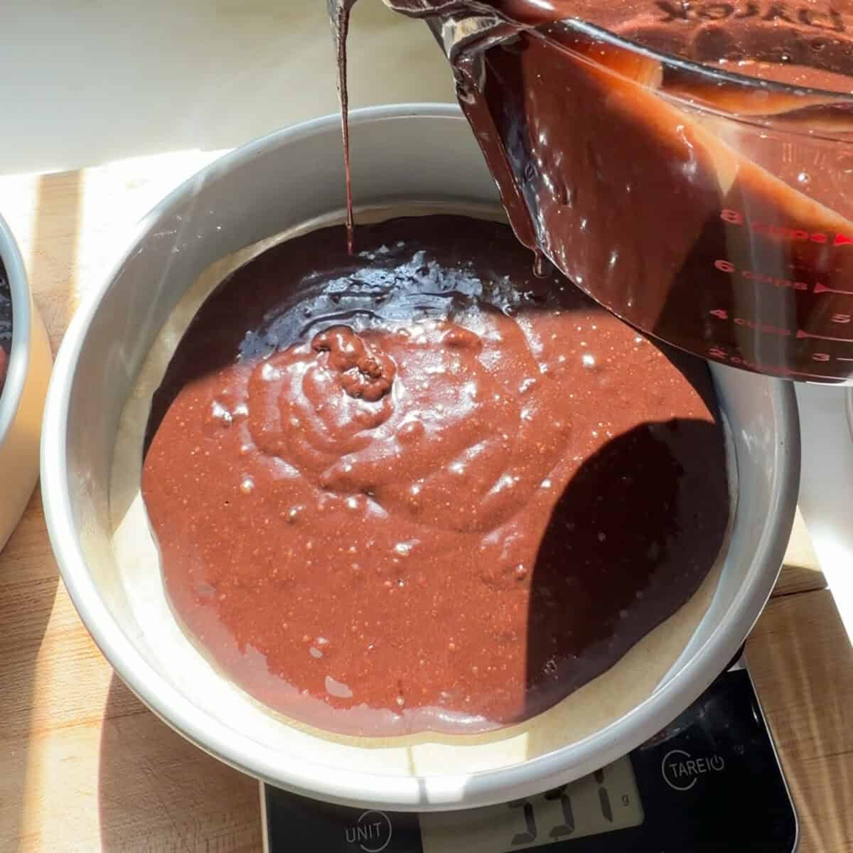 Pouring chocolate cake batter into cake pans.