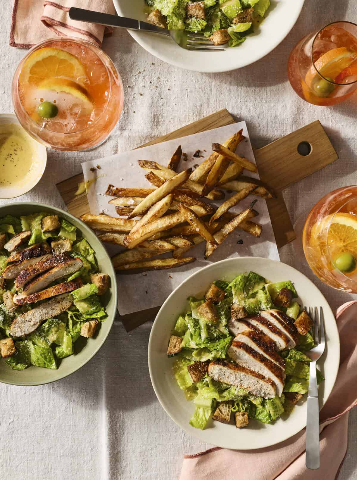 Chicken caesar salad with french fries and aperol spritzs.