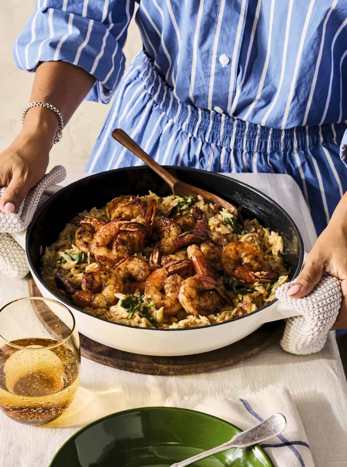 Hands holding skillet of shrimp and orzo.