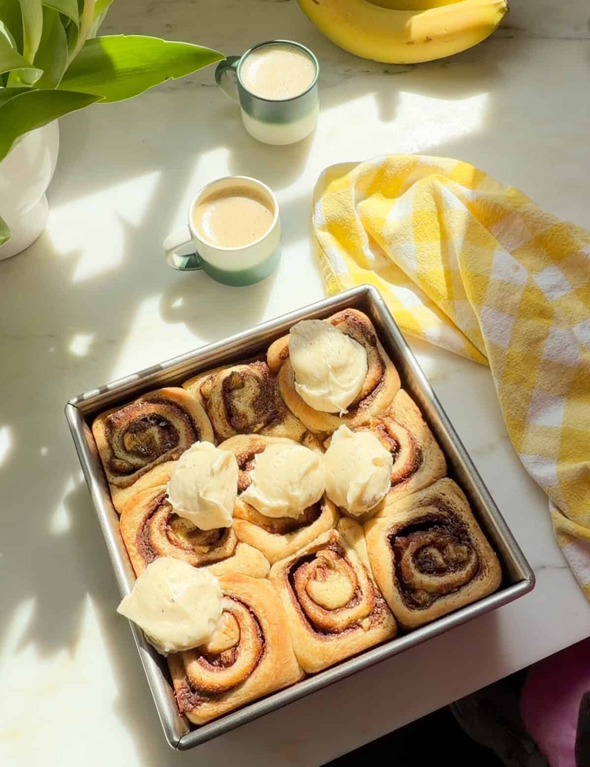 Banana Bread Cinnamon Rolls with scoops of brown butter cream cheese frosting.