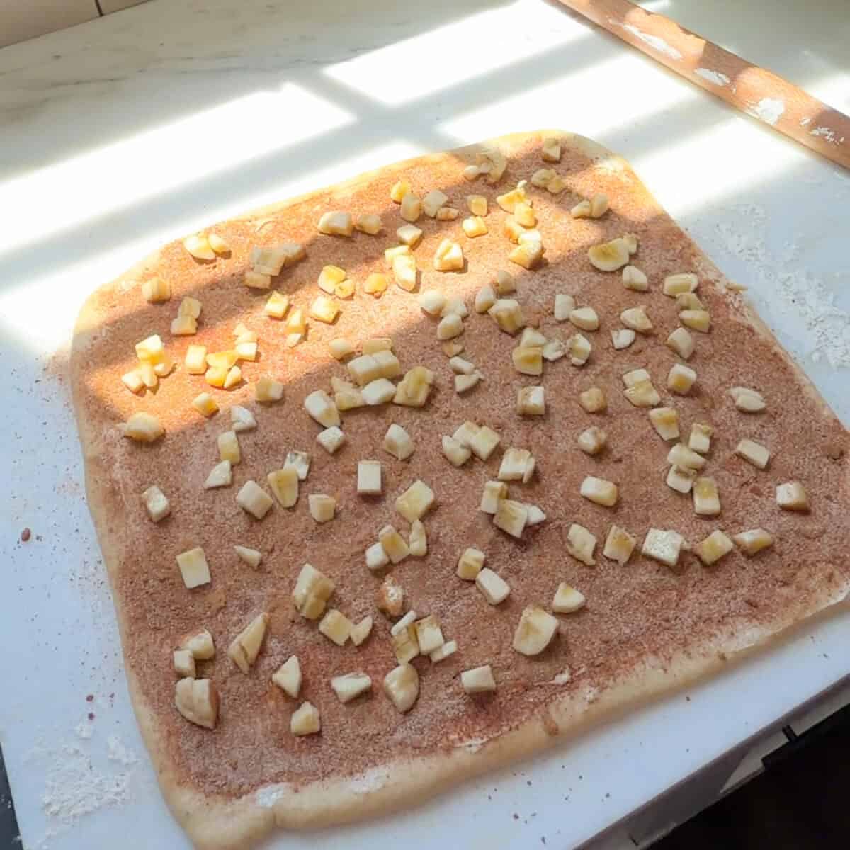 Banana Bread Cinnamon Roll dough with cinnamon sugar and diced banana.