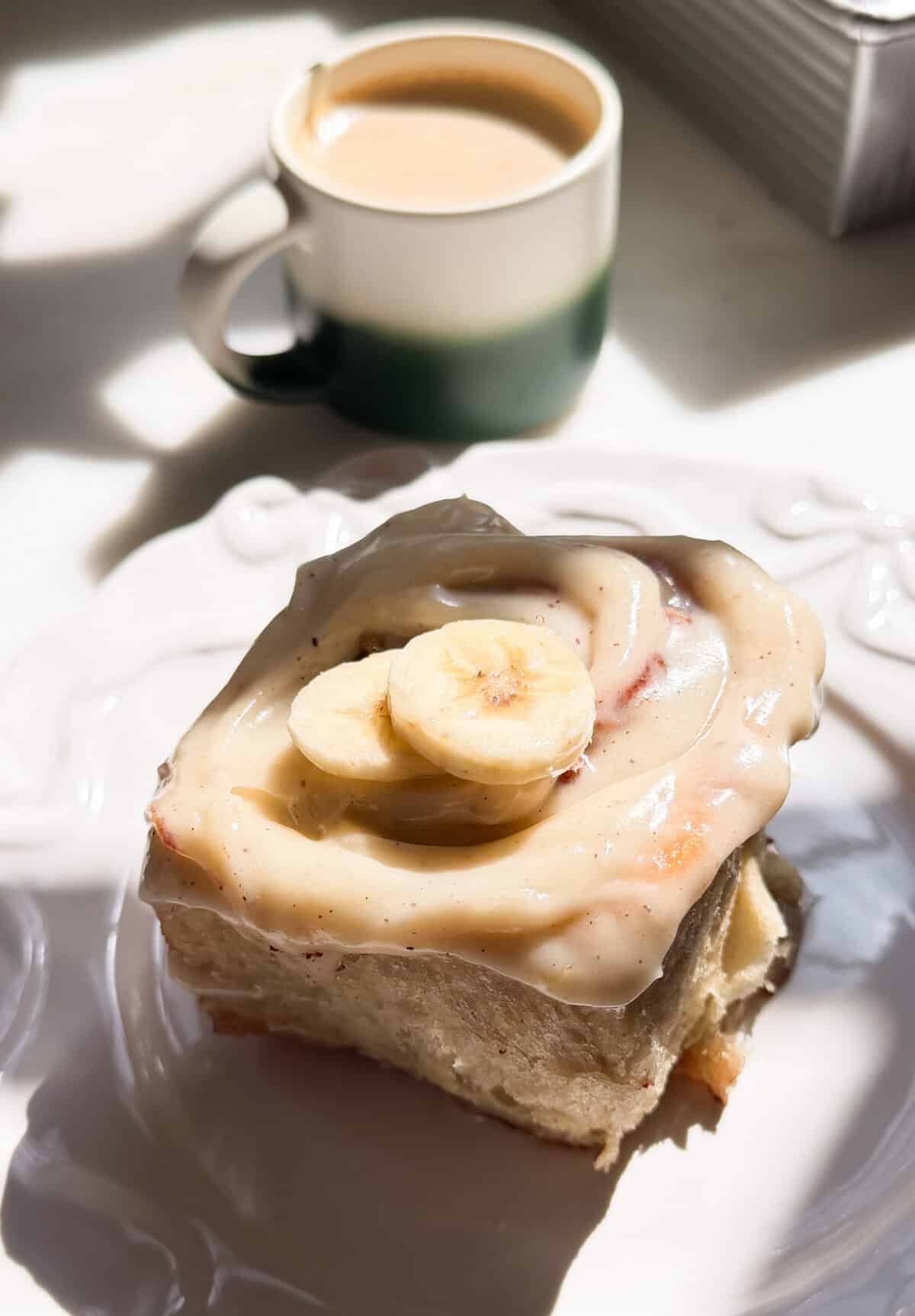 Banana Bread Cinnamon Roll on a plate with a hot coffee.