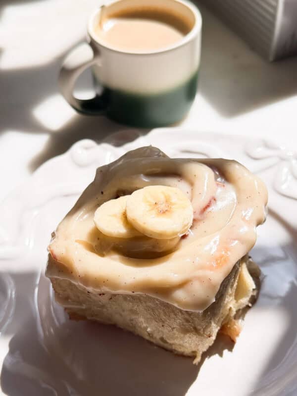 Banana Bread Cinnamon Roll on a plate with a hot coffee.