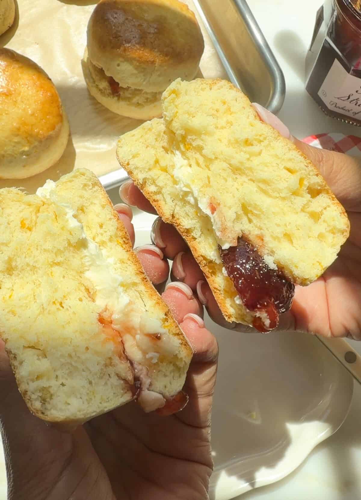 संतरे के स्वाद वाला ब्रिटिश स्कोन, क्लॉटेड क्रीम और आधा टूटा हुआ स्ट्रॉबेरी जैम के साथ।