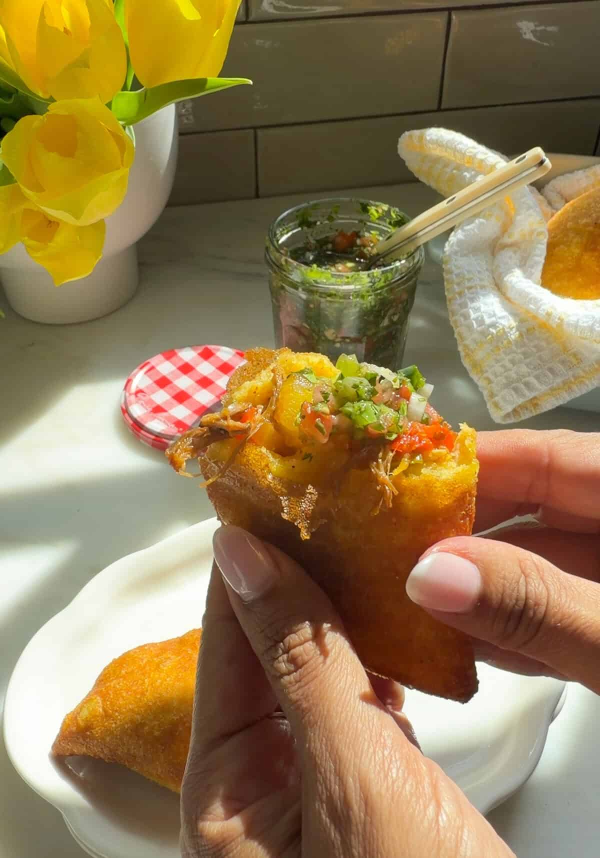 Hands holding Colombian Empanada with aji picante on top.