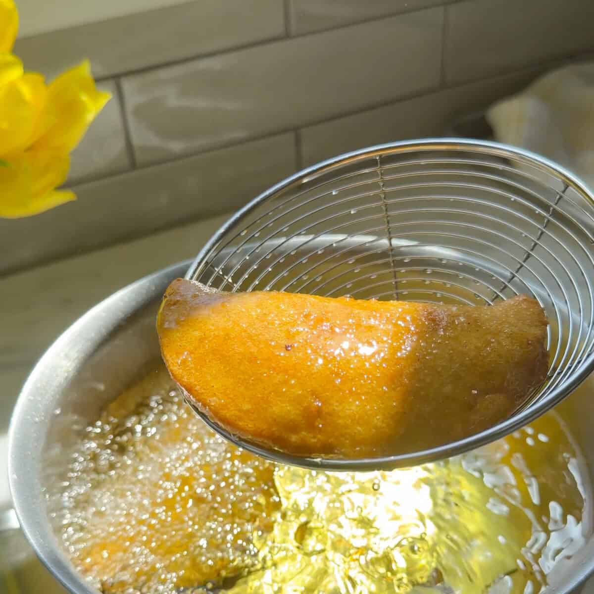 Fried empanada coming out of the hot oil.
