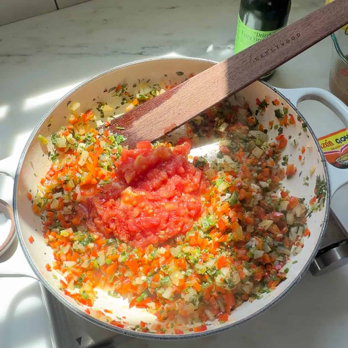 Chopped tomato added to cooked sofrito in skillet.