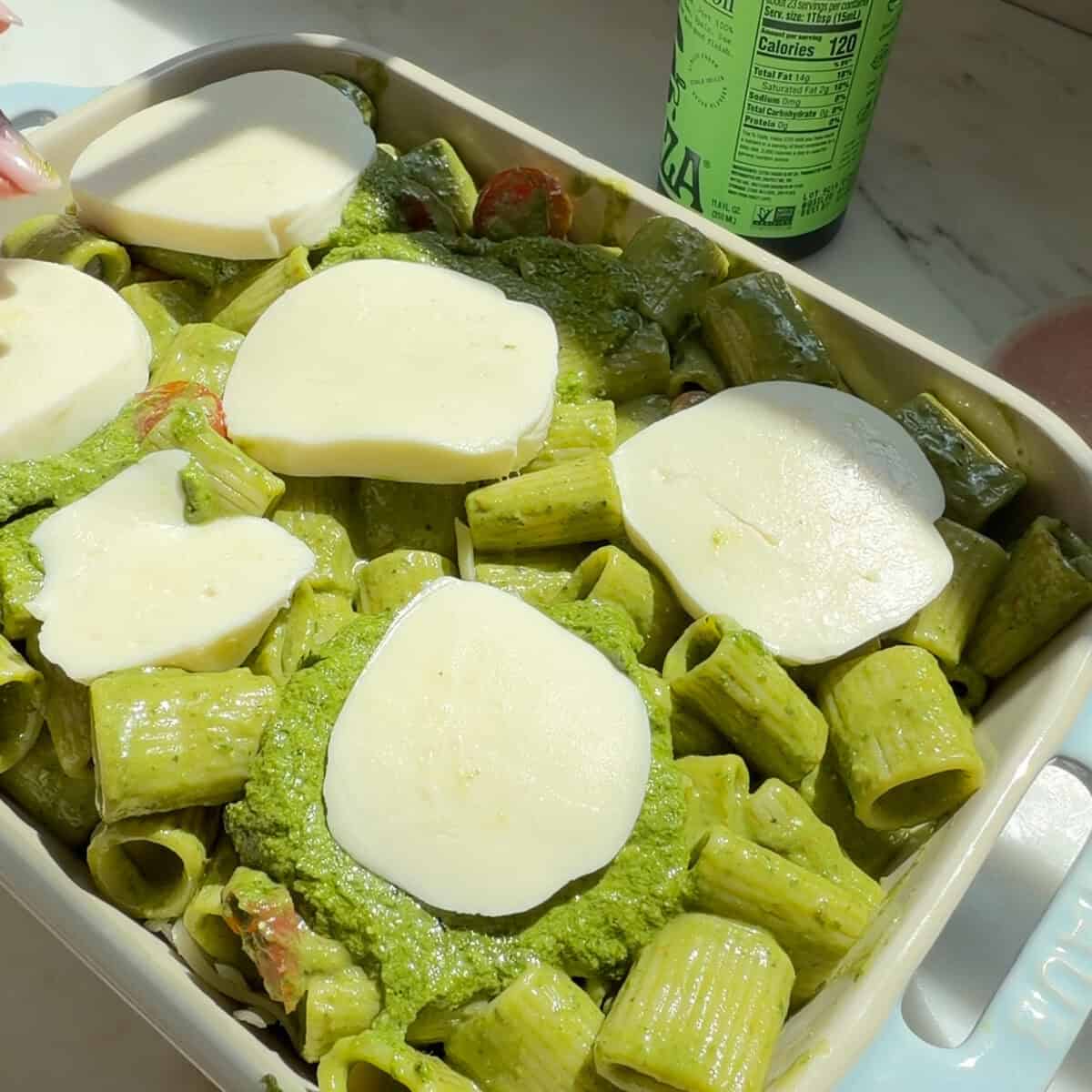 Pesto Pasta with mozzarella slices on top in baking pan.