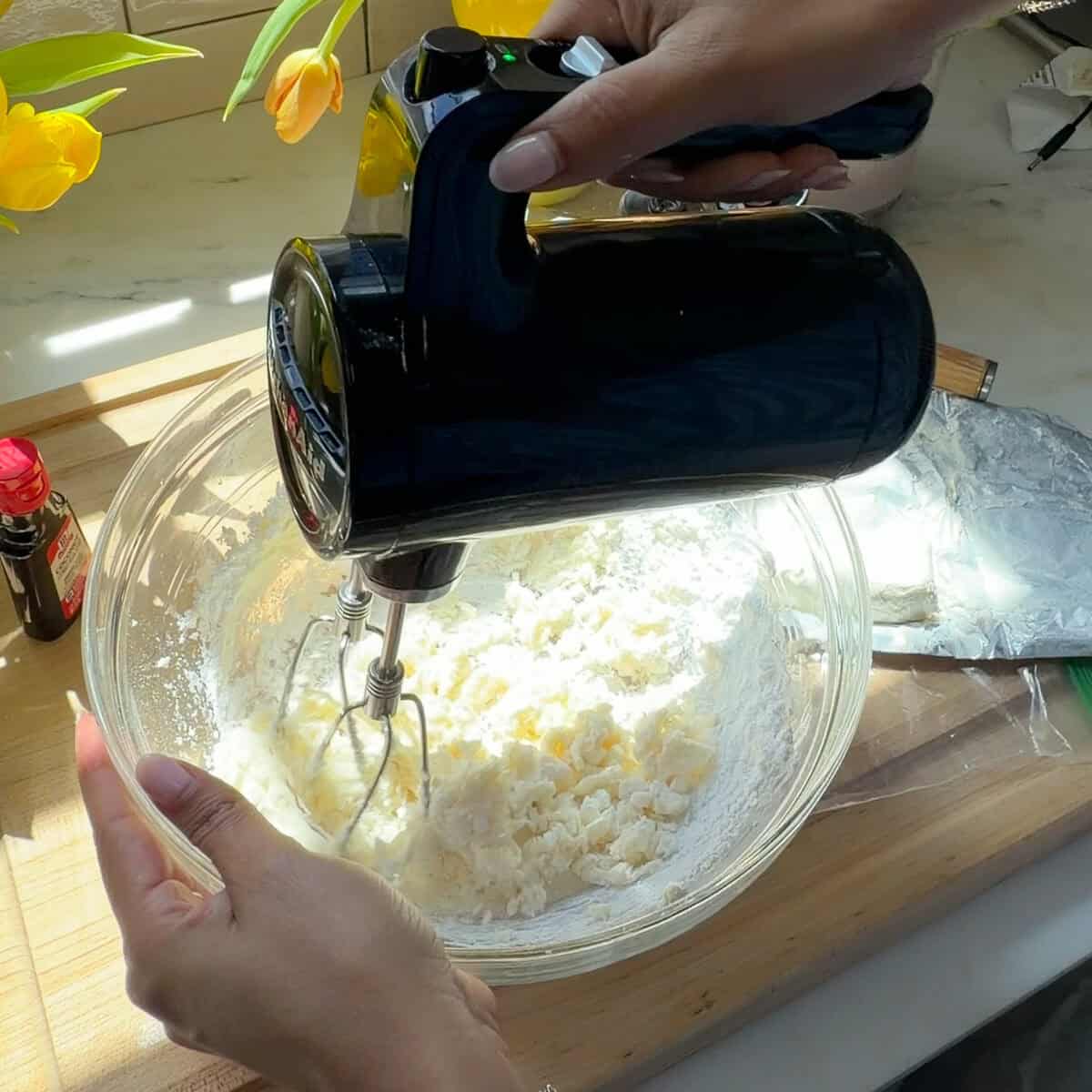Mixing cream cheese frosting with hand mixer.
