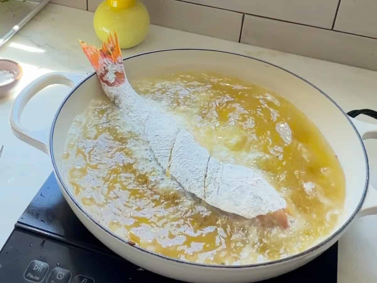 Whole red snapper frying in large braiser.