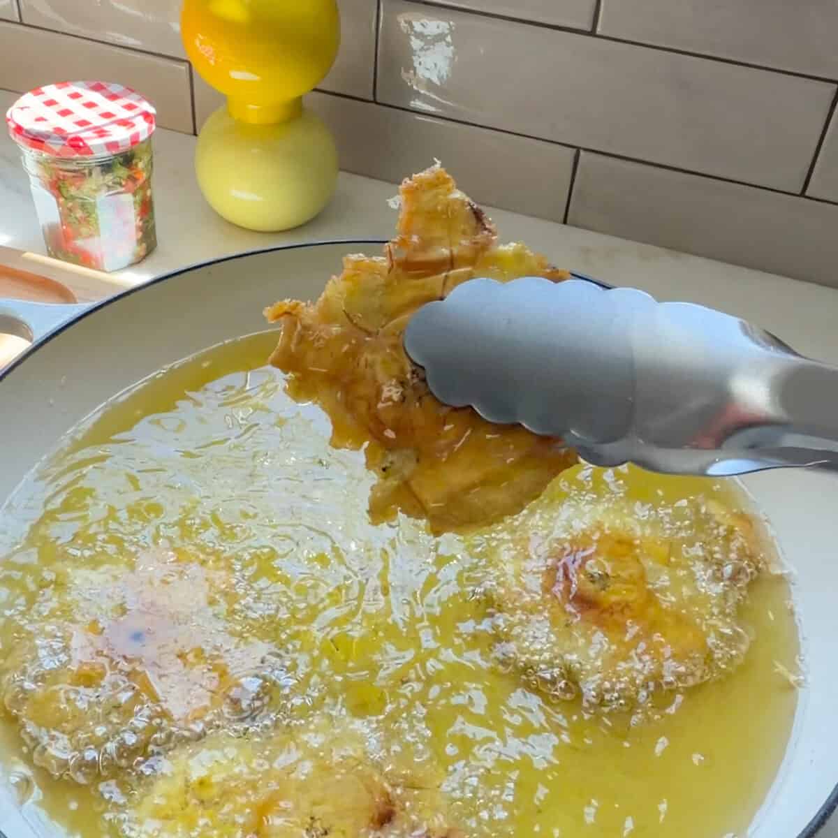 Removing fried tostones from hot oil with tongs.
