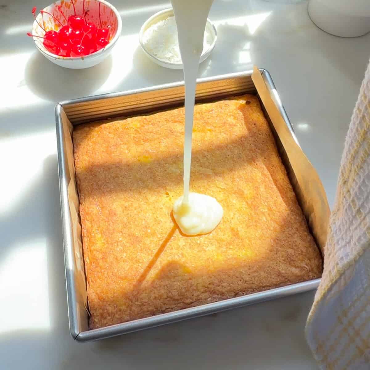 Pouring pineapple white chocolate glaze on baked Piña Colada Brownies.