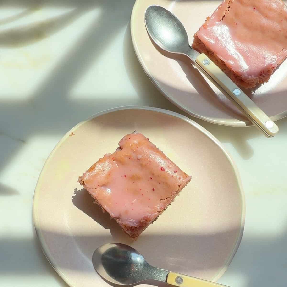 Erdbeer-Brownies mit weißem Schokoladenüberzug 2 Erdbeer-Brownie-Scheiben auf Tellern.